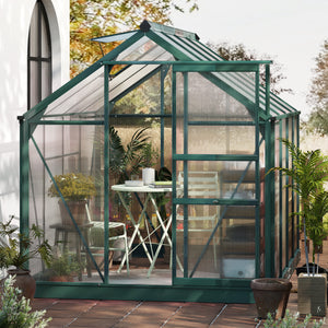 Green greenhouse with a patio area outside, featuring plants and furniture.